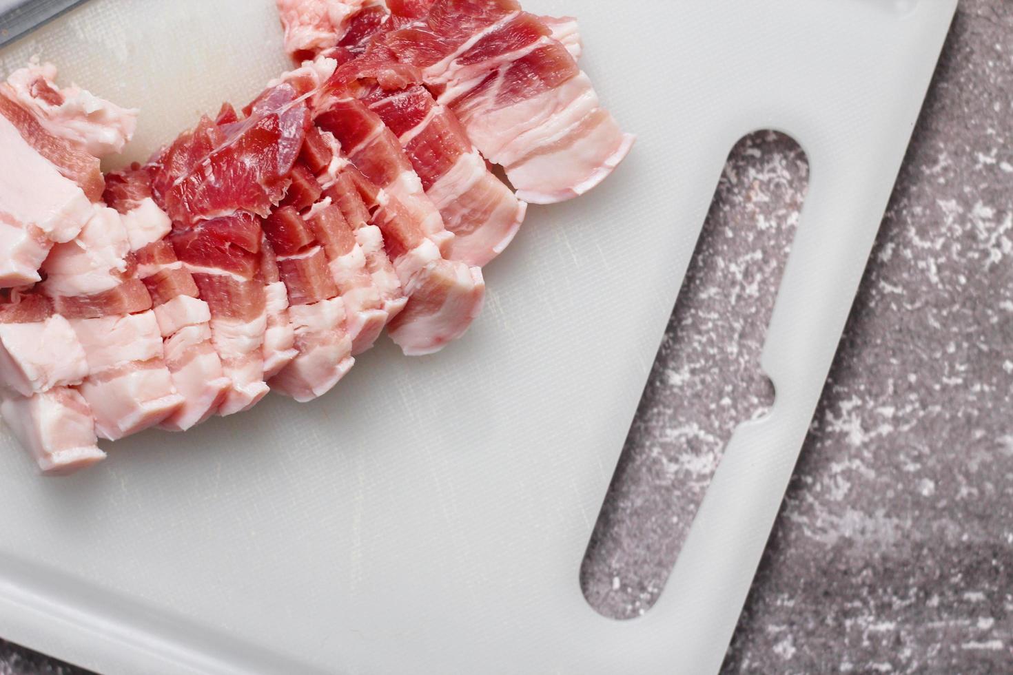 streaky pork is sliced on a white chopping board in the kitchen.Close up cutting slide pork belly raw photo