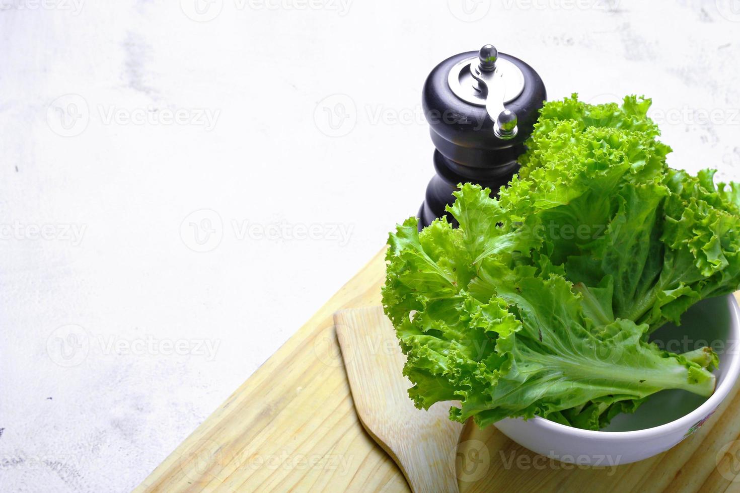 Lettuce placed in a white bowl and a cutting board on a white table. Vegetable salad. Vegetarian food. Clean food. Green vegetables. photo