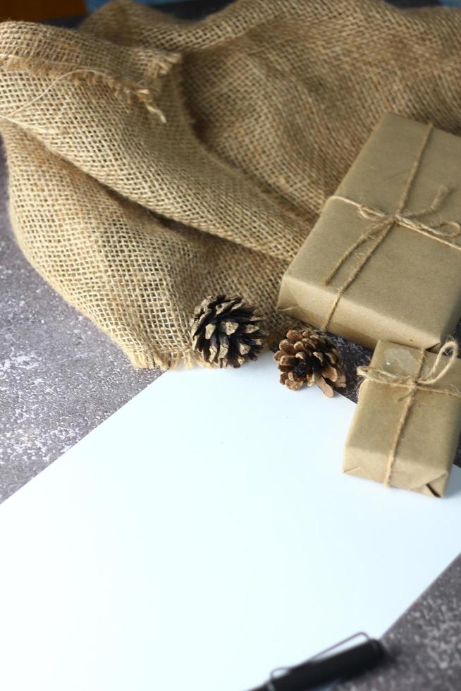 Holidays Gifts. Christmas and New Year.Gift box wrapped in brown paper pine cones and white paper and pens placed on the table, copy space. photo