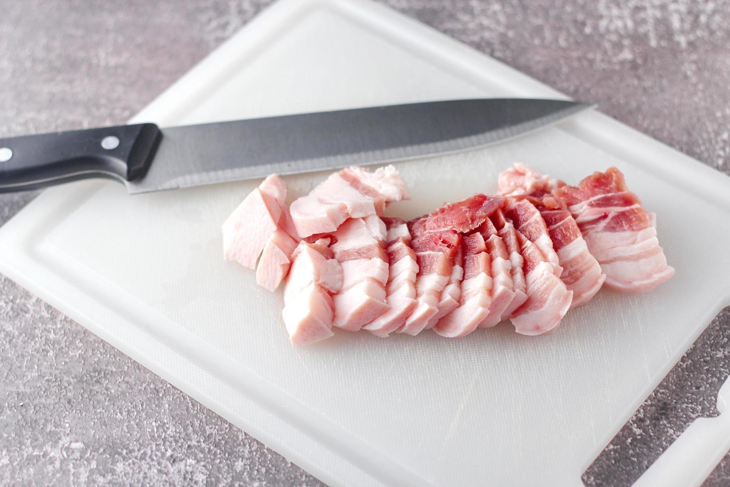 streaky pork is sliced on a white chopping board in the kitchen.Close up cutting slide pork belly raw photo