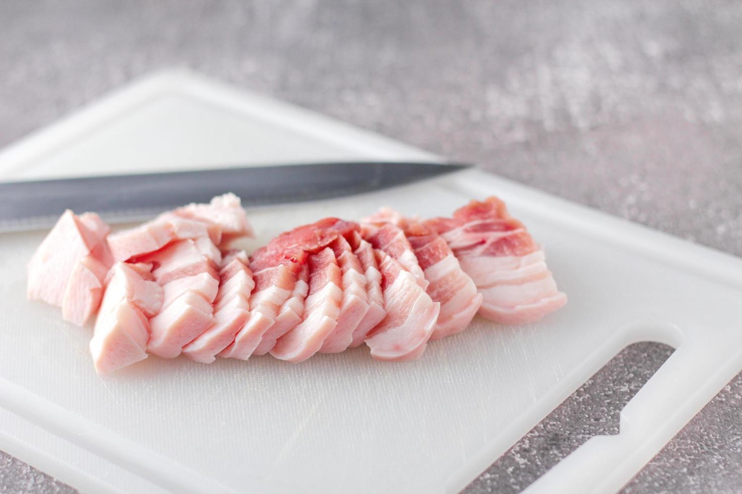 streaky pork is sliced on a white chopping board in the kitchen.Close up cutting slide pork belly raw photo