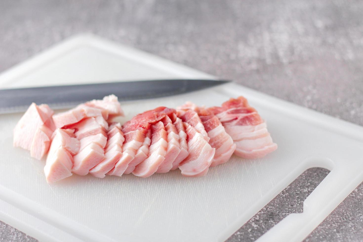 la carne de cerdo rayada se corta en rodajas en una tabla de cortar blanca en la cocina. foto