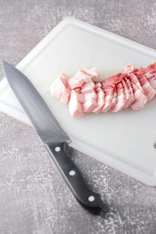 streaky pork is sliced on a white chopping board in the kitchen.Close up cutting slide pork belly raw photo