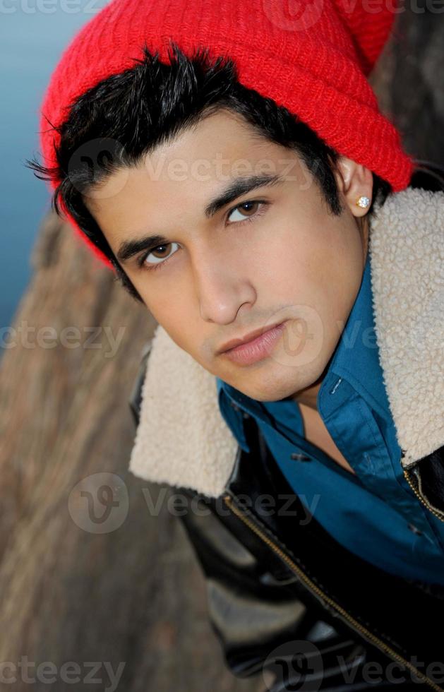 A handsome young hispanic man portrait wearing a ski cap and flight jacket next to a lake in Austin on a cold winters day. photo