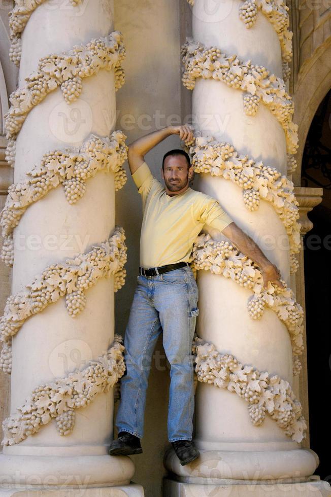 un modelo guapo frente a una columna muy ornamentada posando como un dios griego. foto