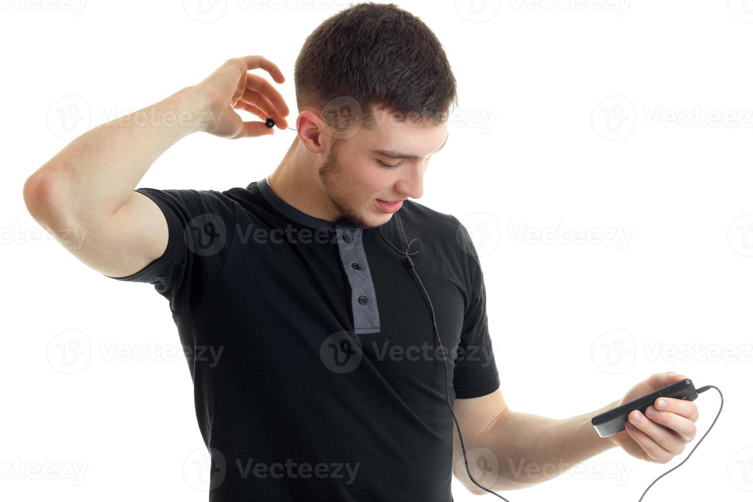 sporty young man in a black t-shirt holding a phone and listening to music with headphones photo