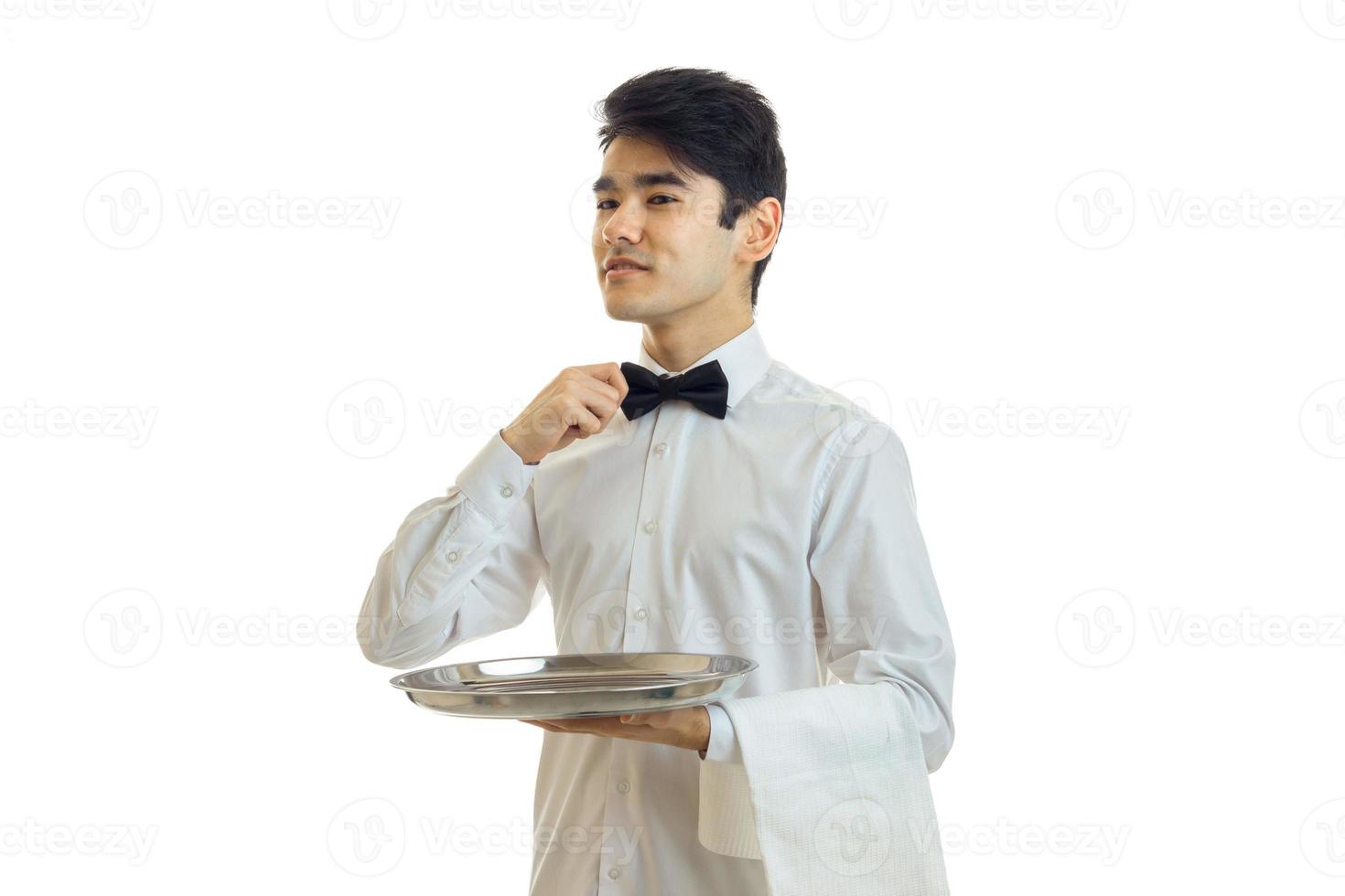 guapo camarero en uniforme con pajarita y bandeja de plata en la mano mirando a un lado foto