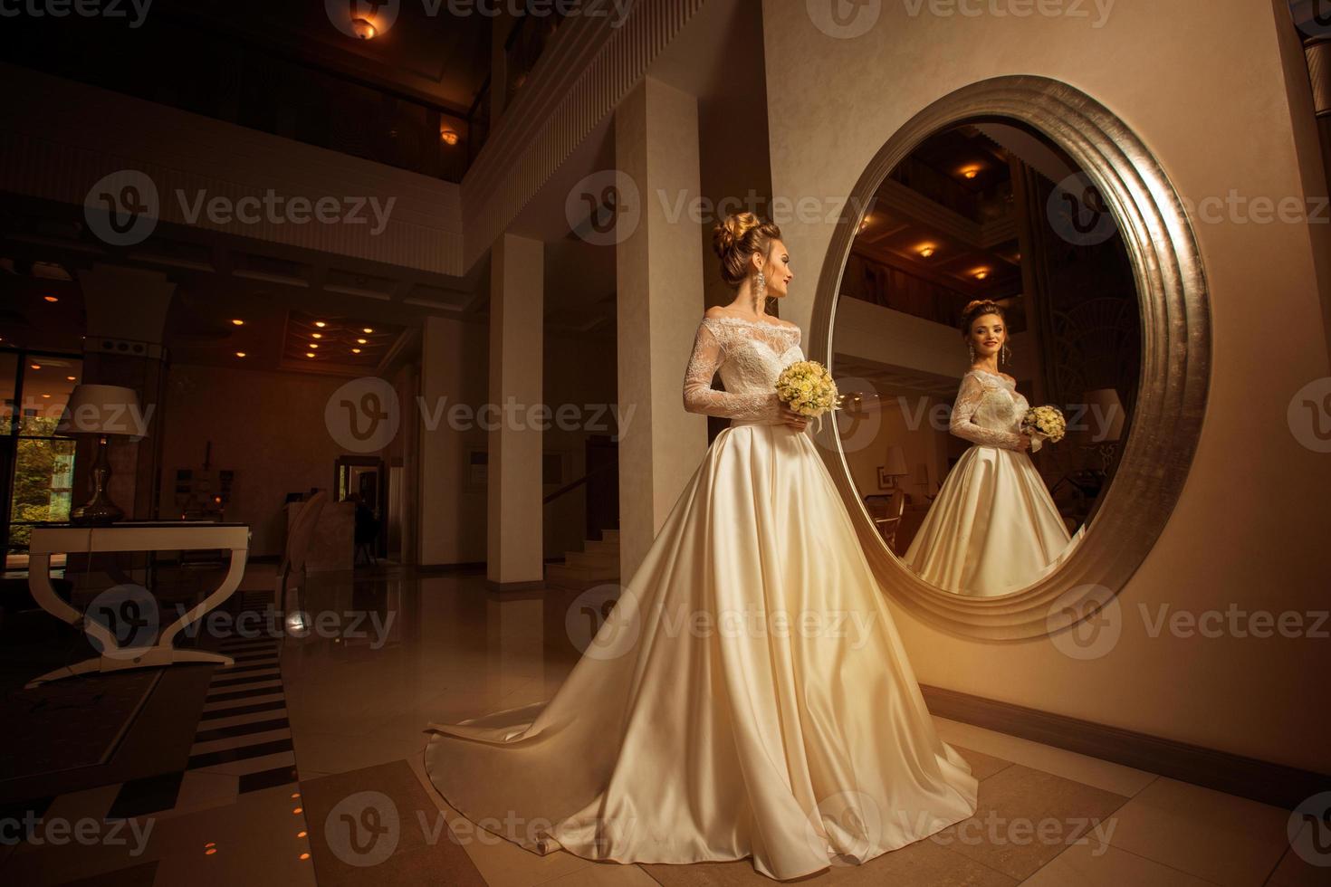 young bride in wedding dress looking at a big mirror photo