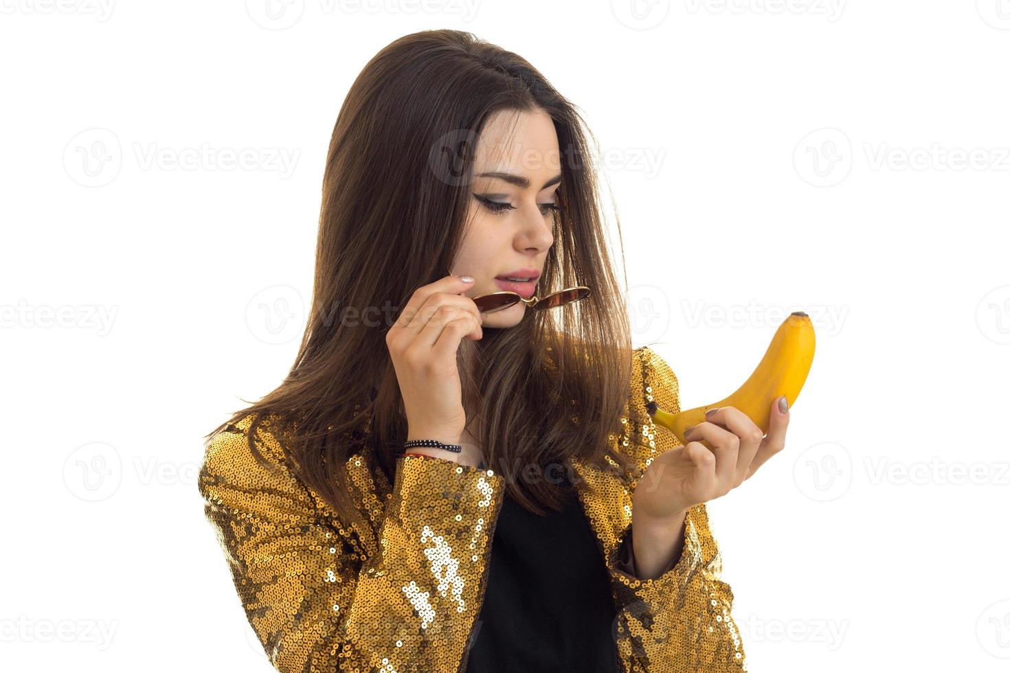 Portrait of a beautiful girl in a bright jacket with glasses and with a banana in her hand isolated on white background photo