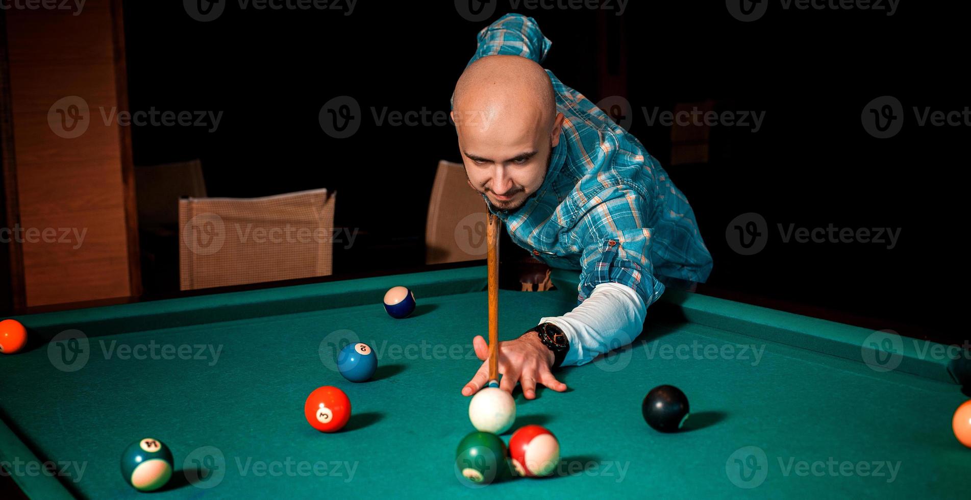 Horizontal portrait of concentrated man plays on billiard table photo
