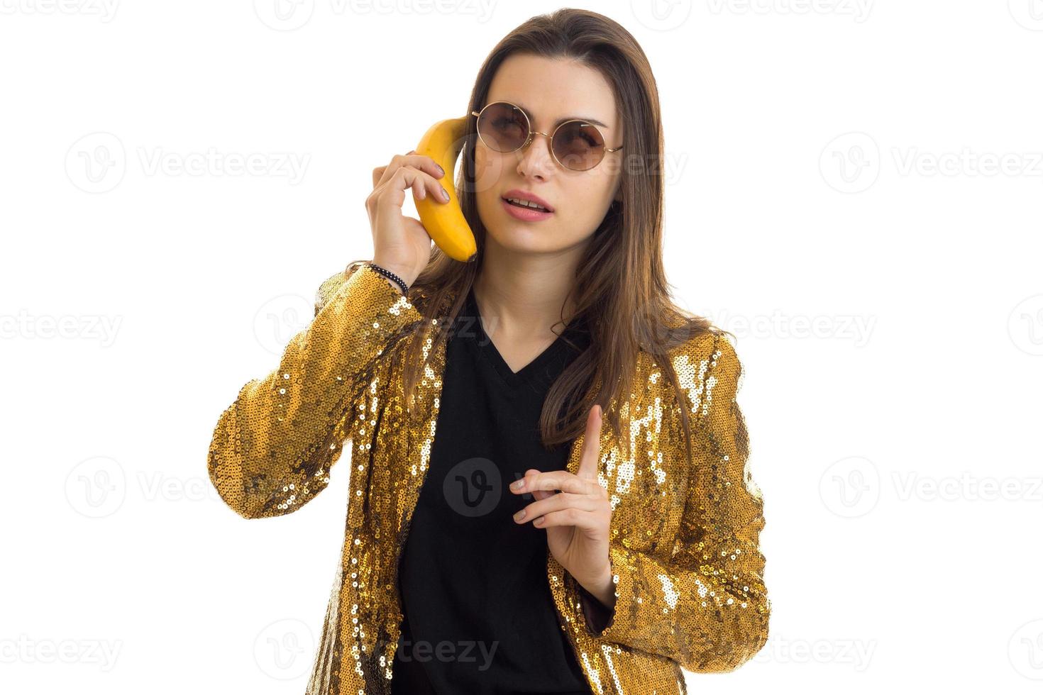 retrato horizontal de chicas jóvenes de moda con gafas redondas en una chaqueta brillante que mantiene el plátano cerca de la oreja foto