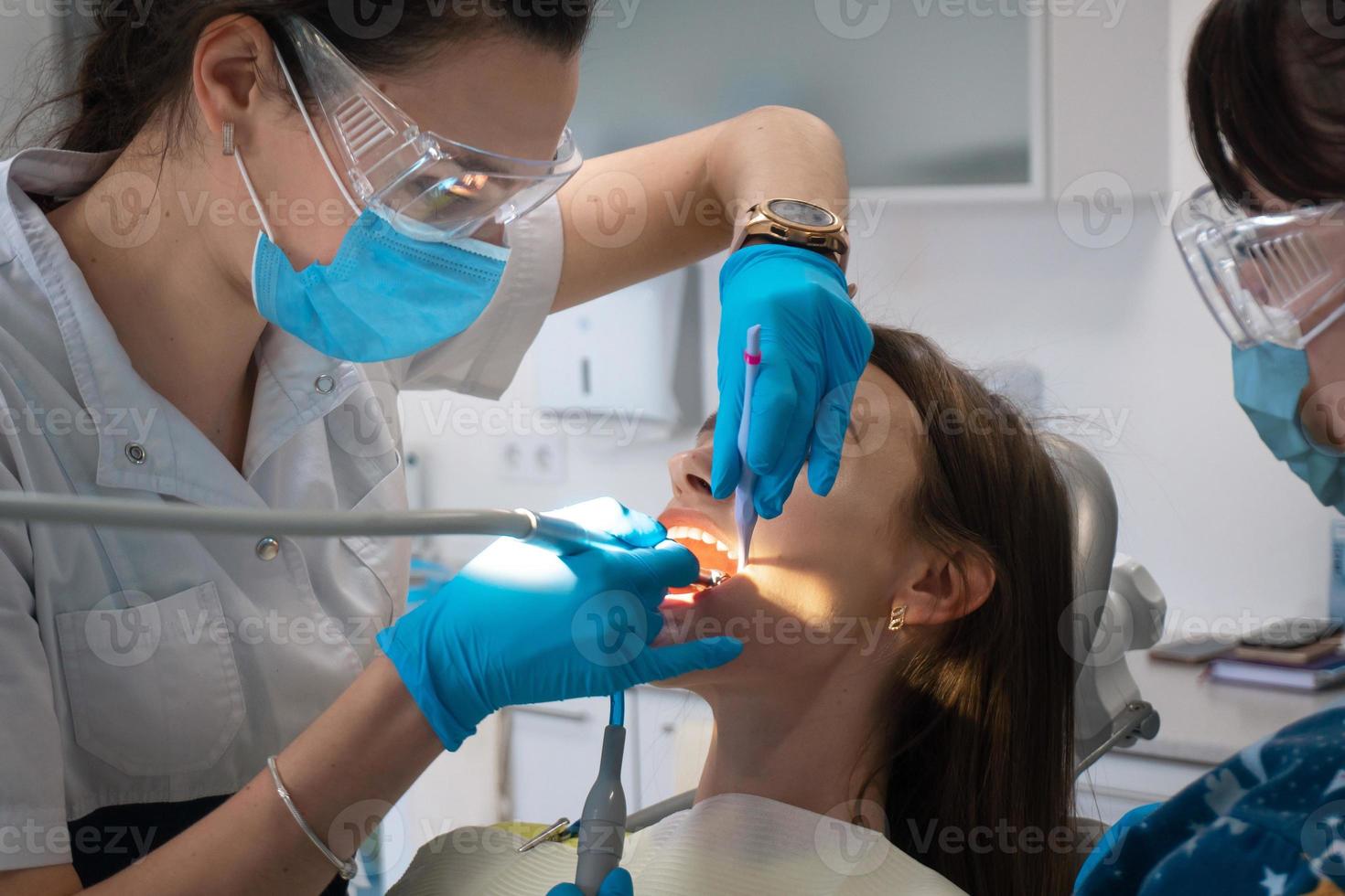 dentista con asistente trata los dientes a una niña en una clínica foto