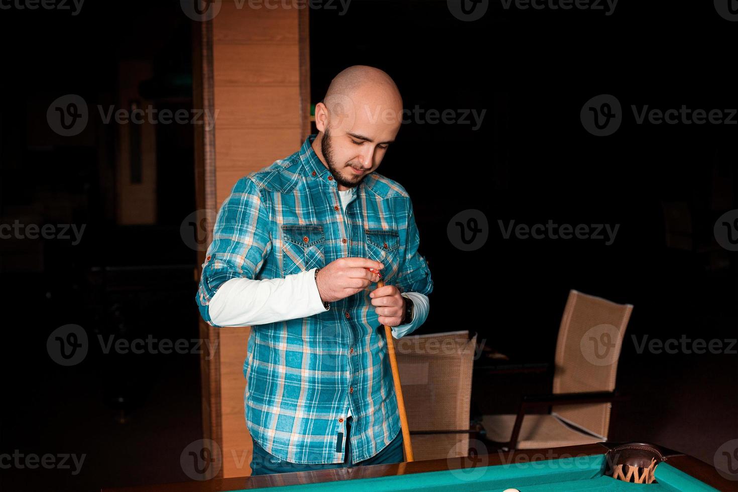 man carefully prepares his cue with chalk to hitting photo