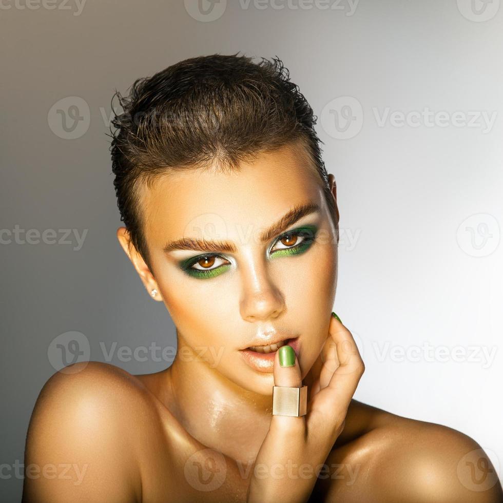 mujer joven glamurosa con maquillaje de colores verdes mirando a la cámara en el estudio foto