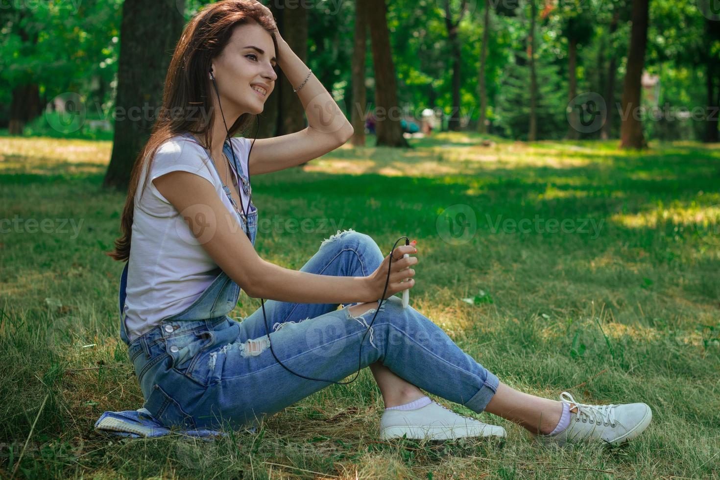 charming pretty girl sitting on the grass in the Park and listens to music photo