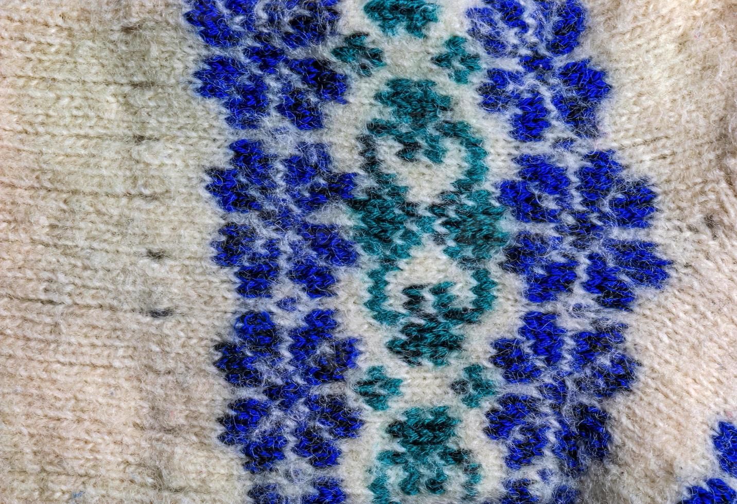 Background of white knitted fabric with blue-green handmade ornament from Argentine merino wool. photo