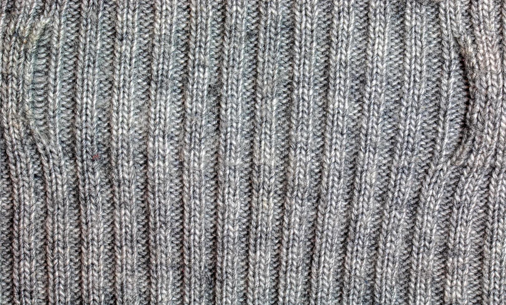 Gray knitted handmade sweater background. The texture of the surface of the woolen jersey made of yarn, close-up. Image for the background. Wool carpet or sweater. Gray texture. Modern design. photo