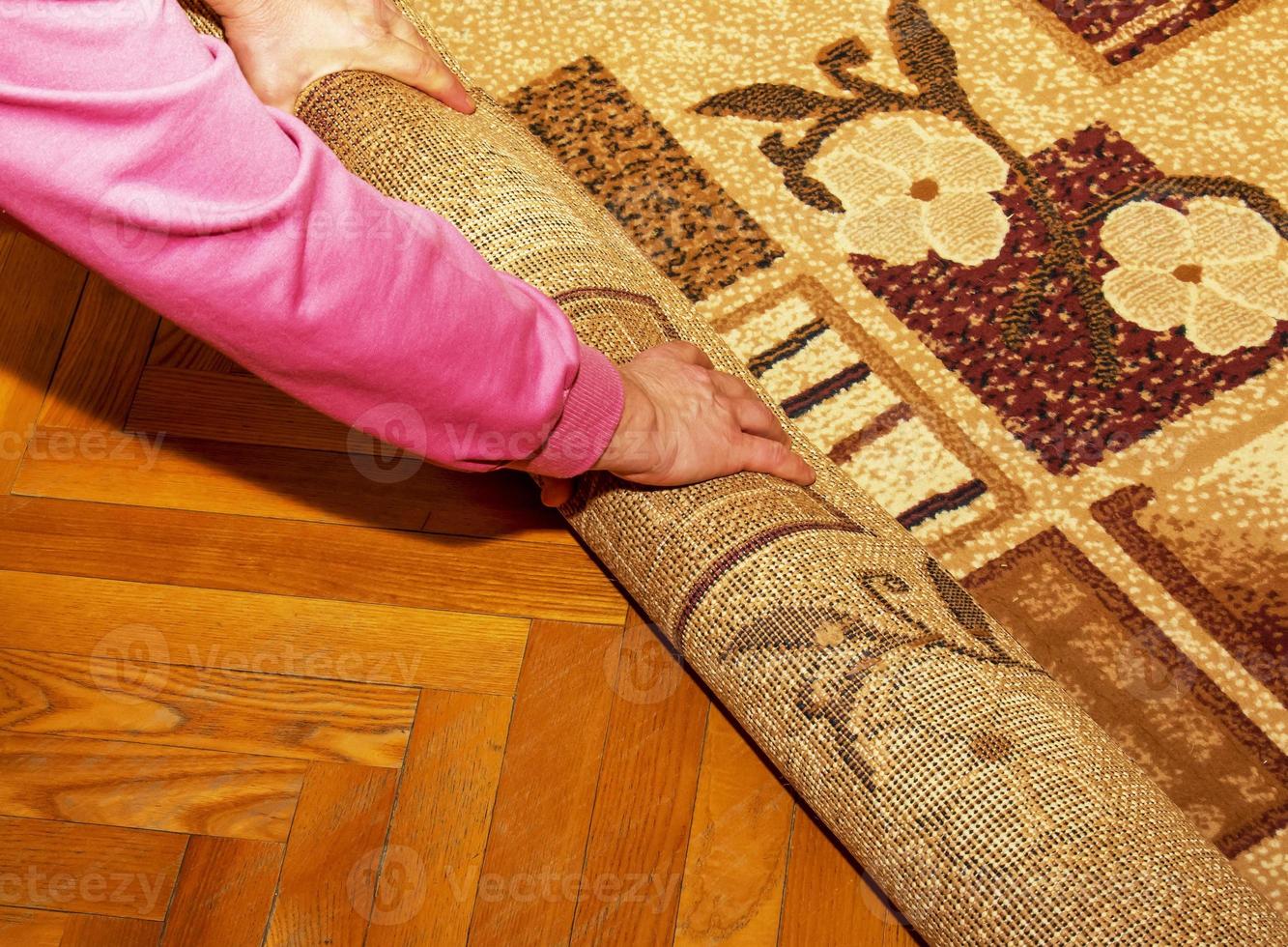 Repair, construction and house concept - close-up of female hands rolling up a carpet. photo