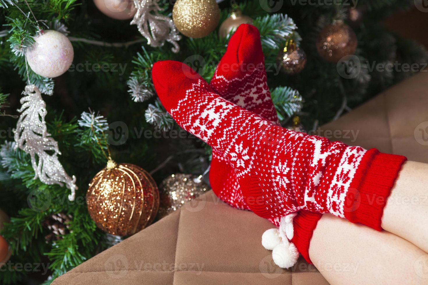 Female feet in red knitted socks and decorated Christmas tree photo