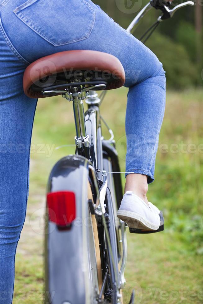 Woman wearing blue jeans sitting on a black bicycle photo