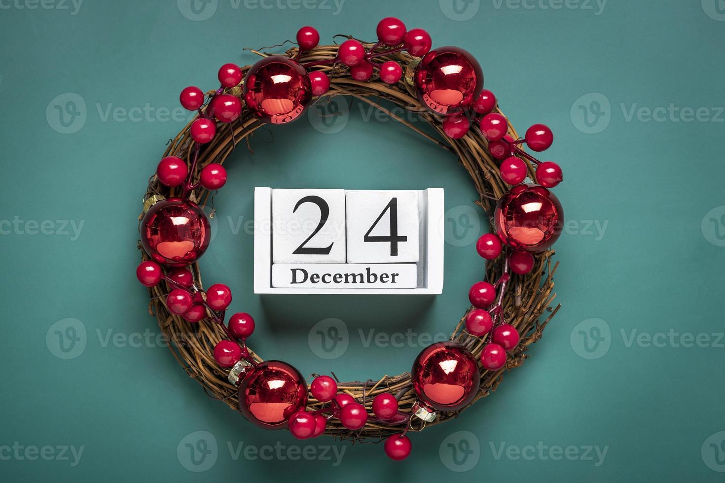 corona de navidad decorada con bayas rojas, calendario de madera fecha 24 de diciembre aislado sobre fondo verde concepto de preparación de navidad, tarjeta de deseos de atmósfera corona de navidad hecha a mano plana foto