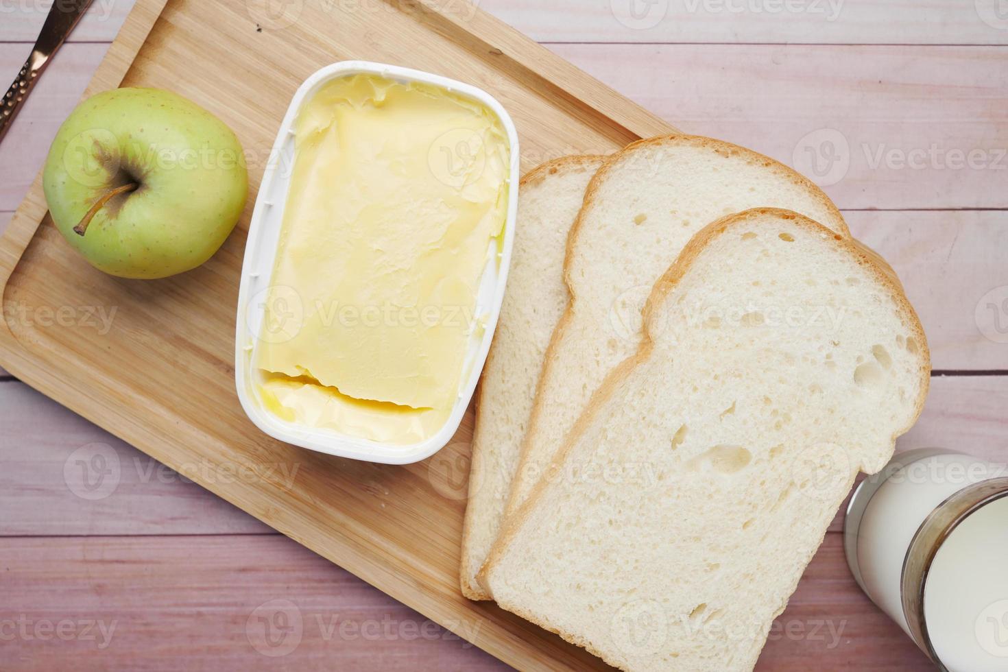 fresh butter in a container with bread, apple and milk on table photo