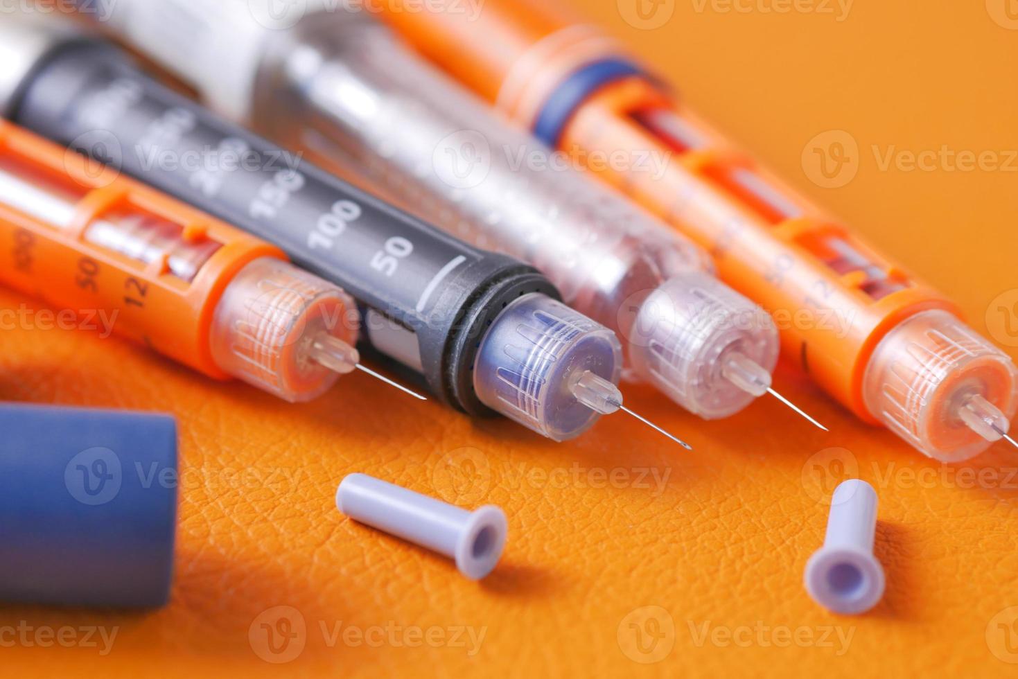 Insulin pens on orange background, close up photo