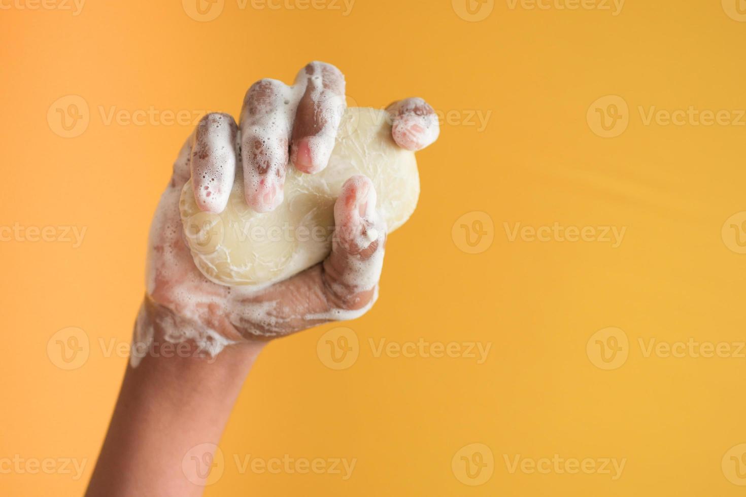 young man washing hands with soap on yellow background photo