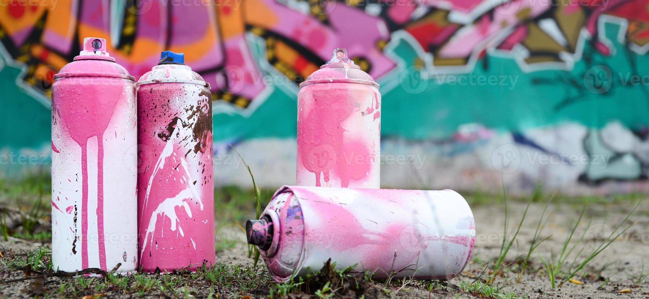 A few used paint cans lie on the ground near the wall with a beautiful graffiti painting in pink and green colors. Street art concept photo