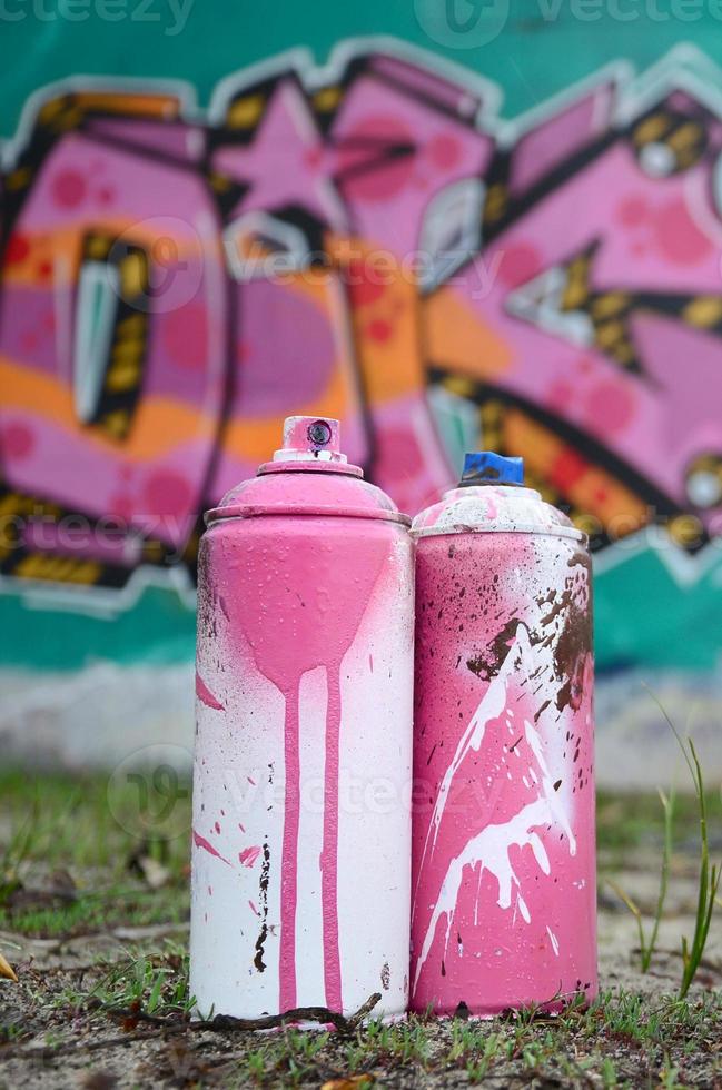 A few used paint cans lie on the ground near the wall with a beautiful graffiti painting in pink and green colors. Street art concept photo