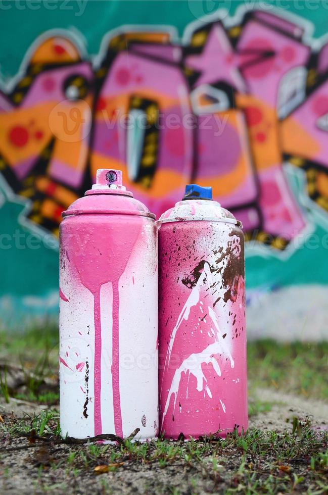 A few used paint cans lie on the ground near the wall with a beautiful graffiti painting in pink and green colors. Street art concept photo