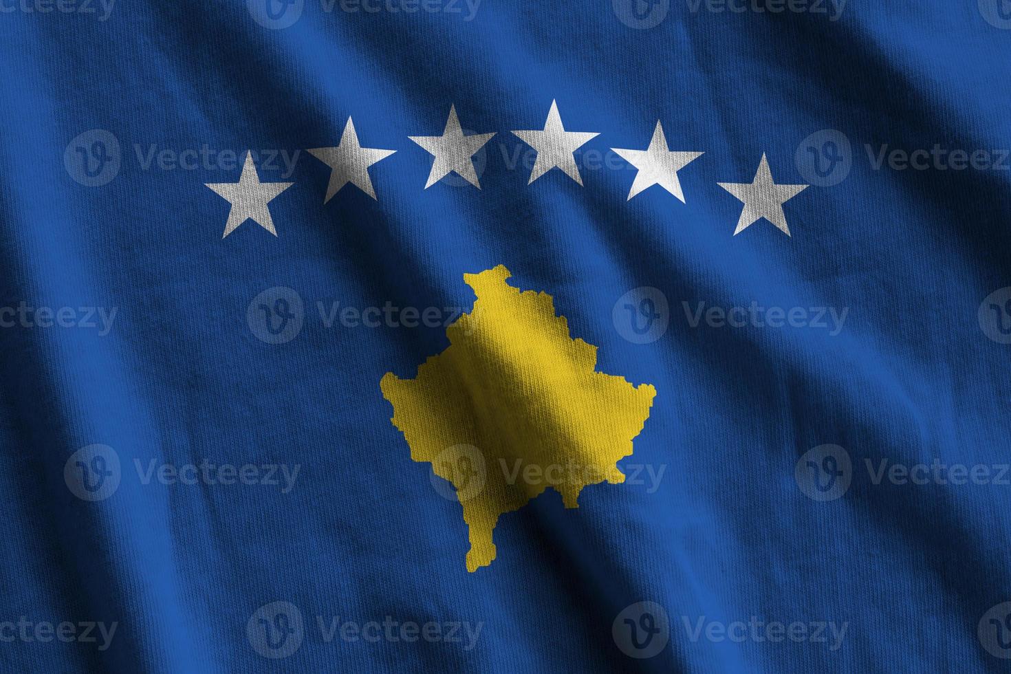 Kosovo flag with big folds waving close up under the studio light indoors. The official symbols and colors in banner photo