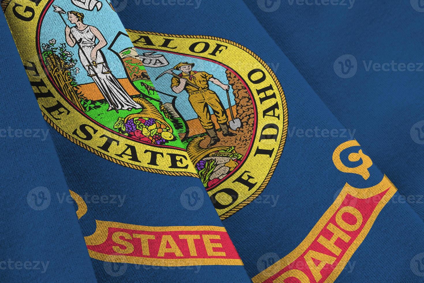 Idaho US state flag with big folds waving close up under the studio light indoors. The official symbols and colors in banner photo