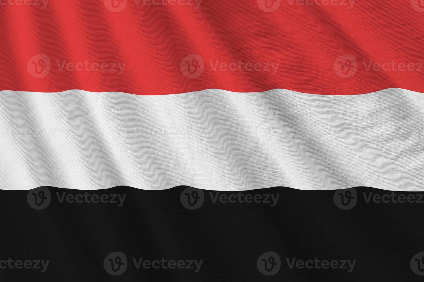 Yemen flag with big folds waving close up under the studio light indoors. The official symbols and colors in banner photo