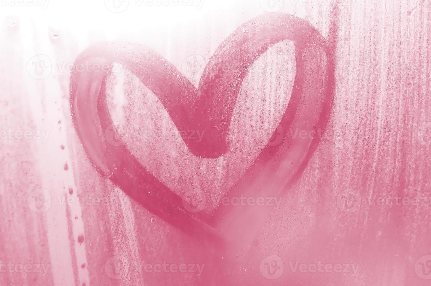 A heart-shaped drawing drawn by a finger on a misted glass in rainy weather Image toned in Viva Magenta, color of the year photo