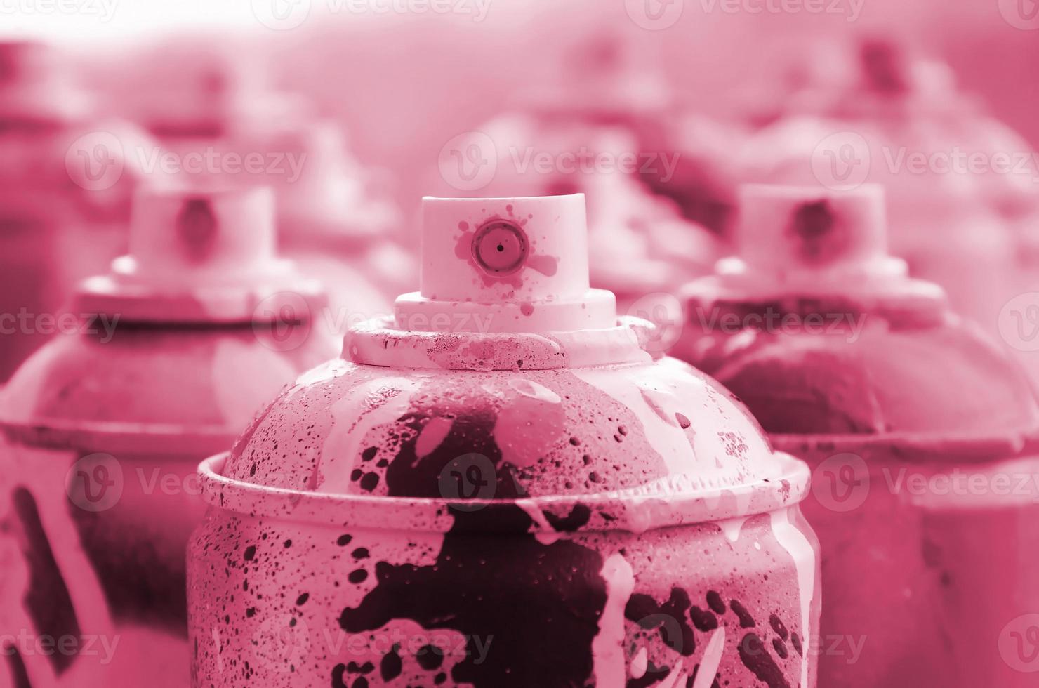 A lot of dirty and used aerosol cans of paint. Macro photograph with shallow depth of field. Selective focus on the spray nozzle Image toned in Viva Magenta, color of the 2023 year photo