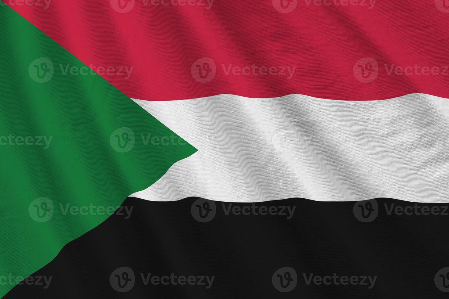 Sudan flag with big folds waving close up under the studio light indoors. The official symbols and colors in banner photo
