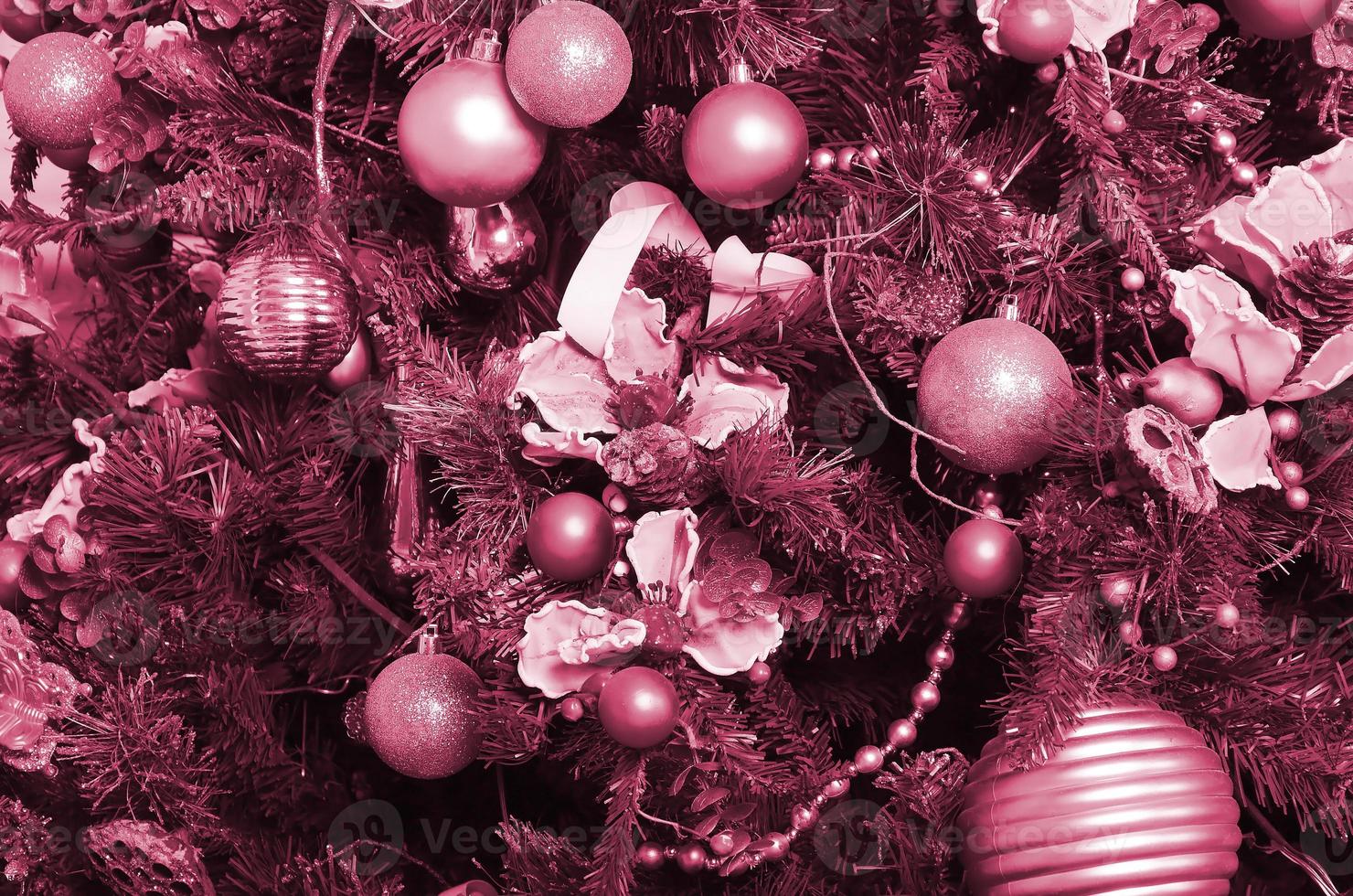 Decorating Christmas tree close up. Decoration bulb, green fir tree, golden x-mas toys and lights. Use for Christmas and New years celebration Image toned in Viva Magenta, color of the 2023 year photo
