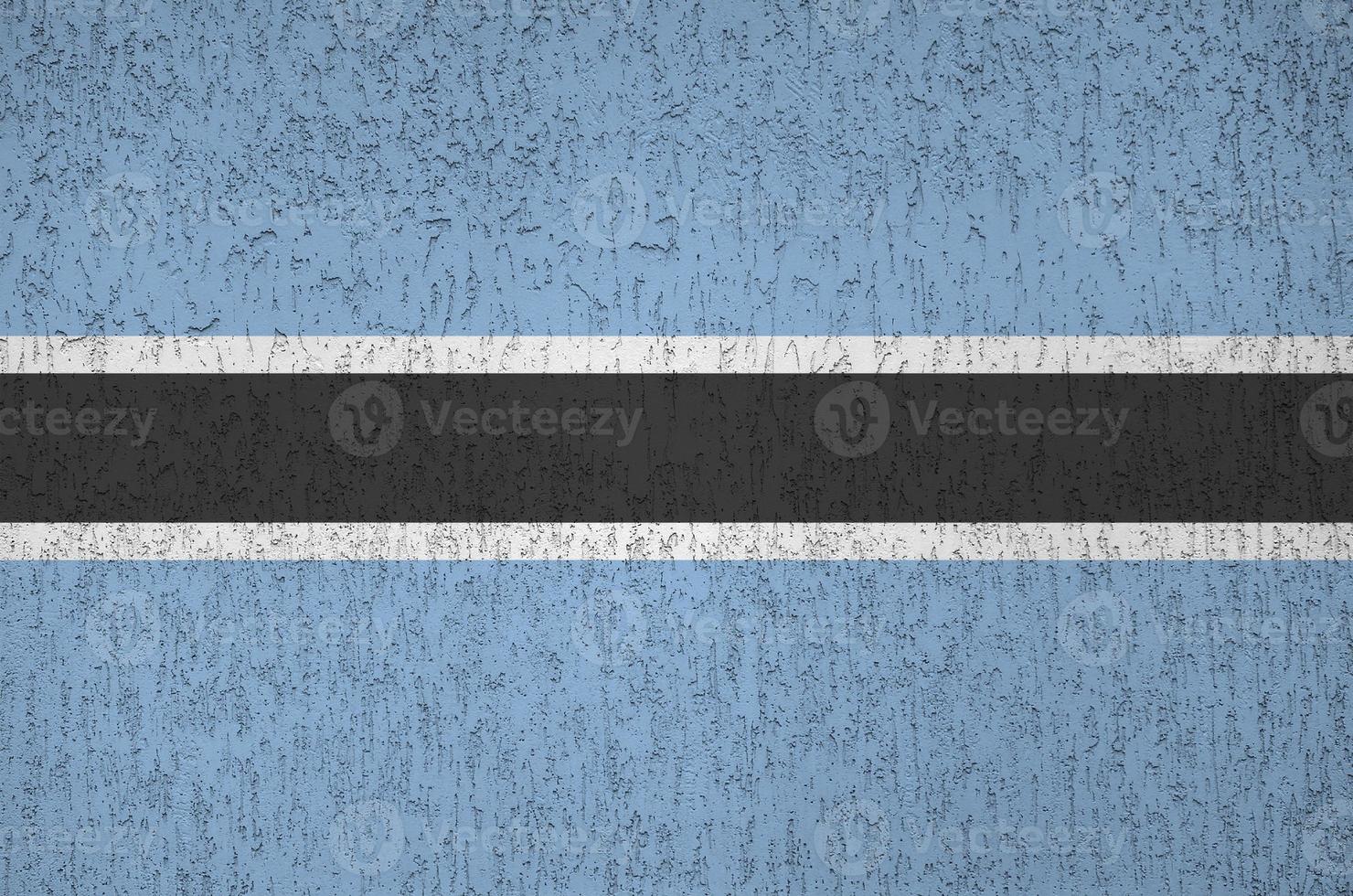 Botswana flag depicted in bright paint colors on old relief plastering wall. Textured banner on rough background photo