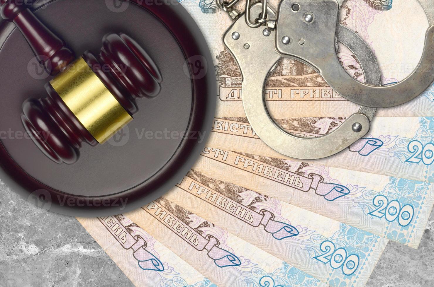 200 Ukrainian hryvnias bills and judge hammer with police handcuffs on court desk. Concept of judicial trial or bribery. Tax avoidance photo