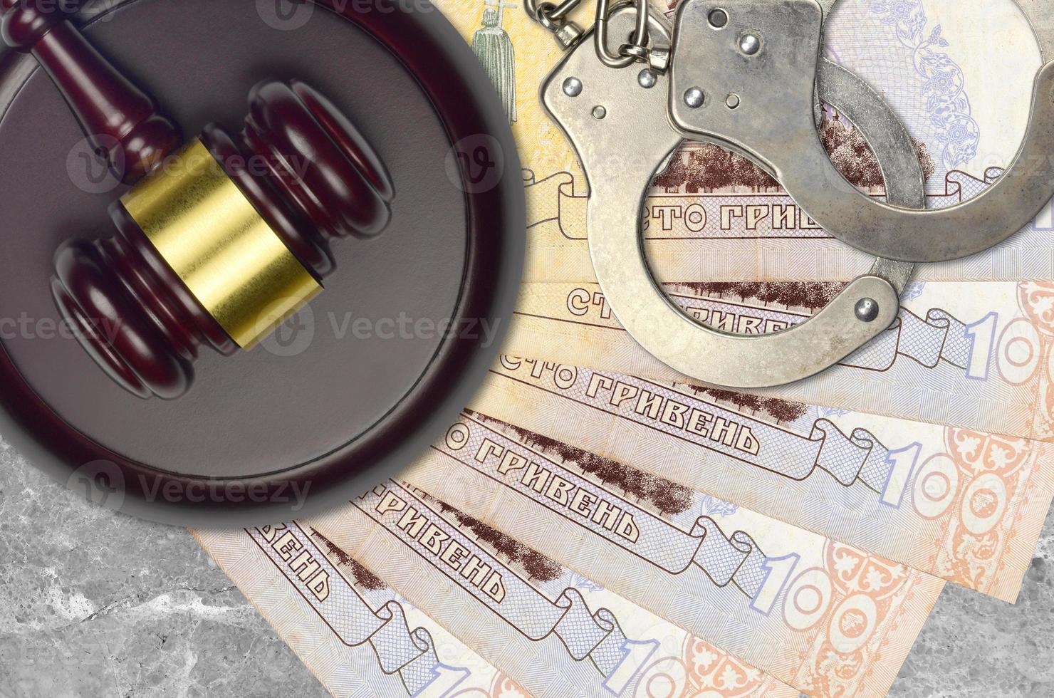 100 Ukrainian hryvnias bills and judge hammer with police handcuffs on court desk. Concept of judicial trial or bribery. Tax avoidance photo