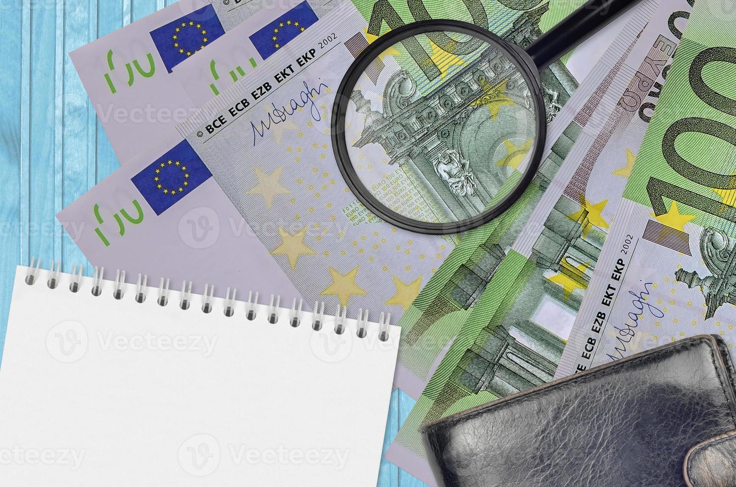 100 Euro bills and magnifying glass with black purse and notepad. Concept of counterfeit money. Search for differences in details on money bills to detect fake photo