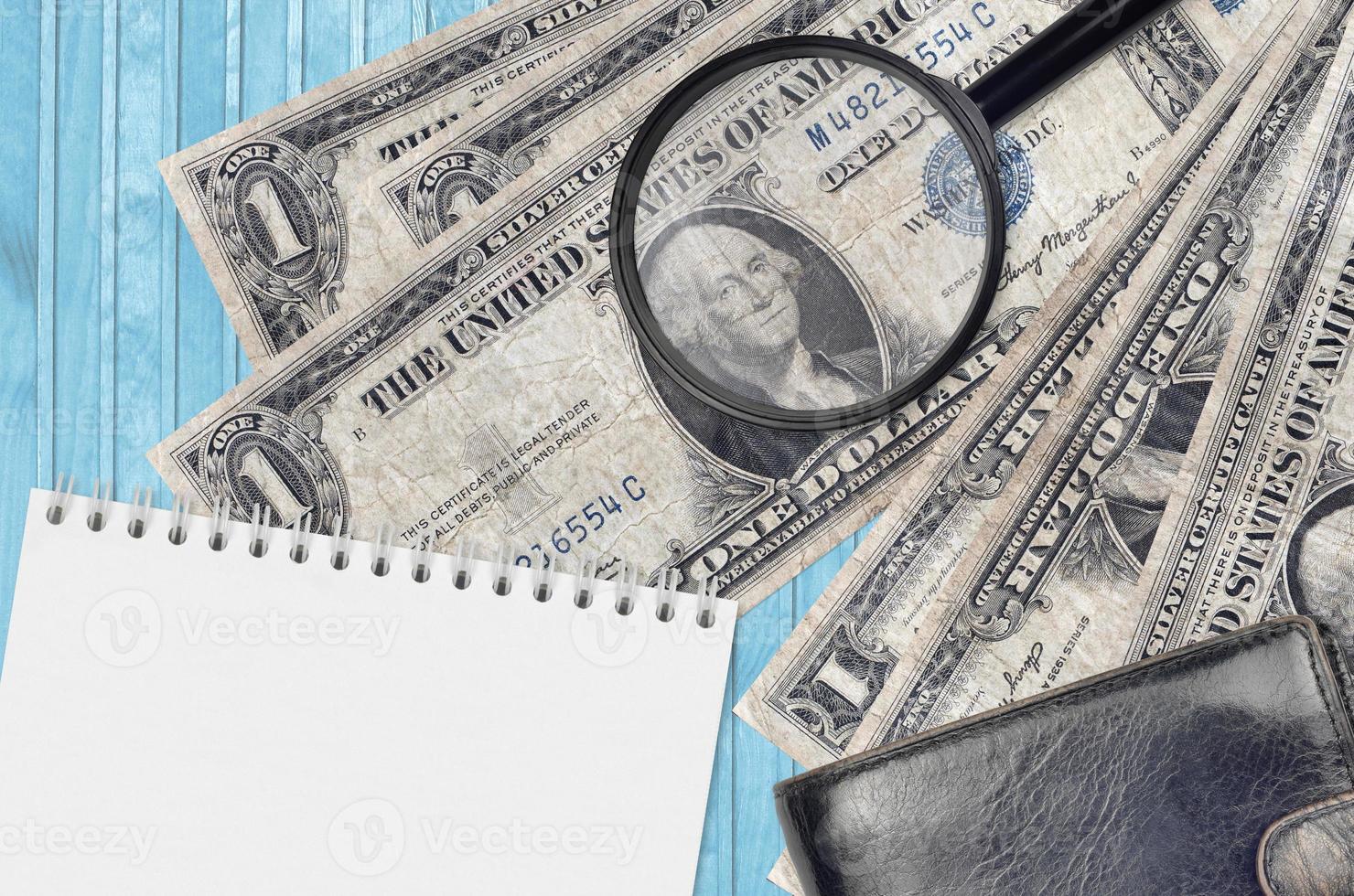 1 US dollar bills and magnifying glass with black purse and notepad. Concept of counterfeit money. Search for differences in details on money bills to detect fake photo