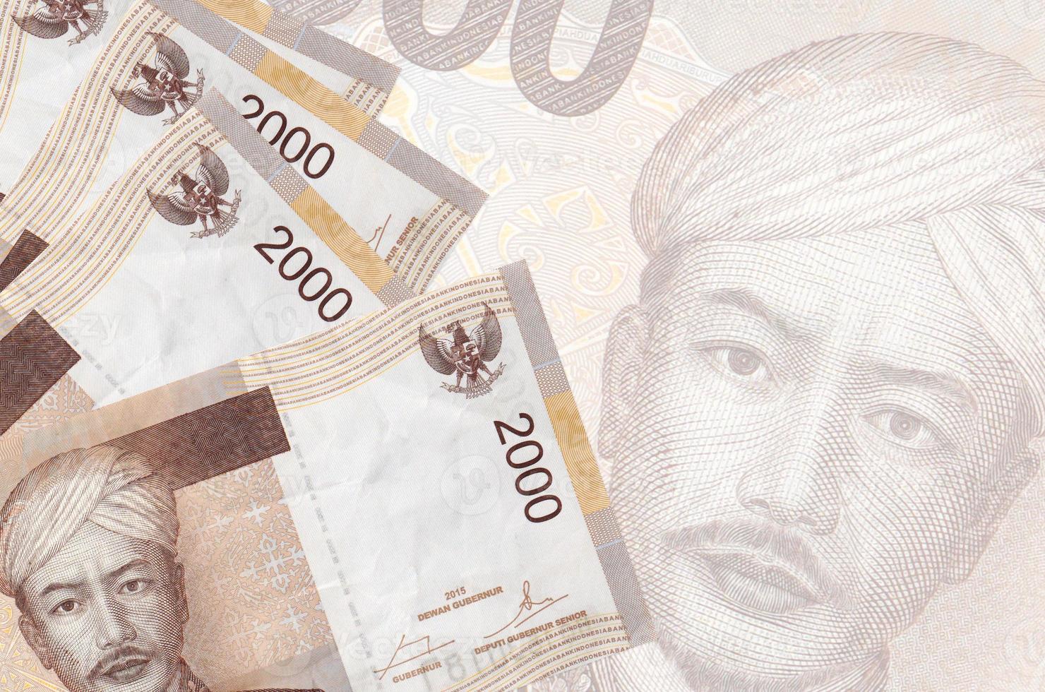 Los billetes de 2000 rupias indonesias se encuentran apilados sobre el fondo de un gran billete semitransparente. fondo de negocios abstracto foto
