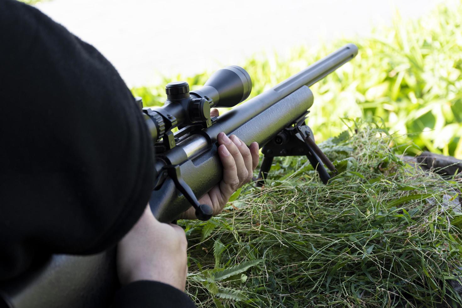 vista superior hombre vestido con capucha negra está disparando rifle mirando a través del alcance foto