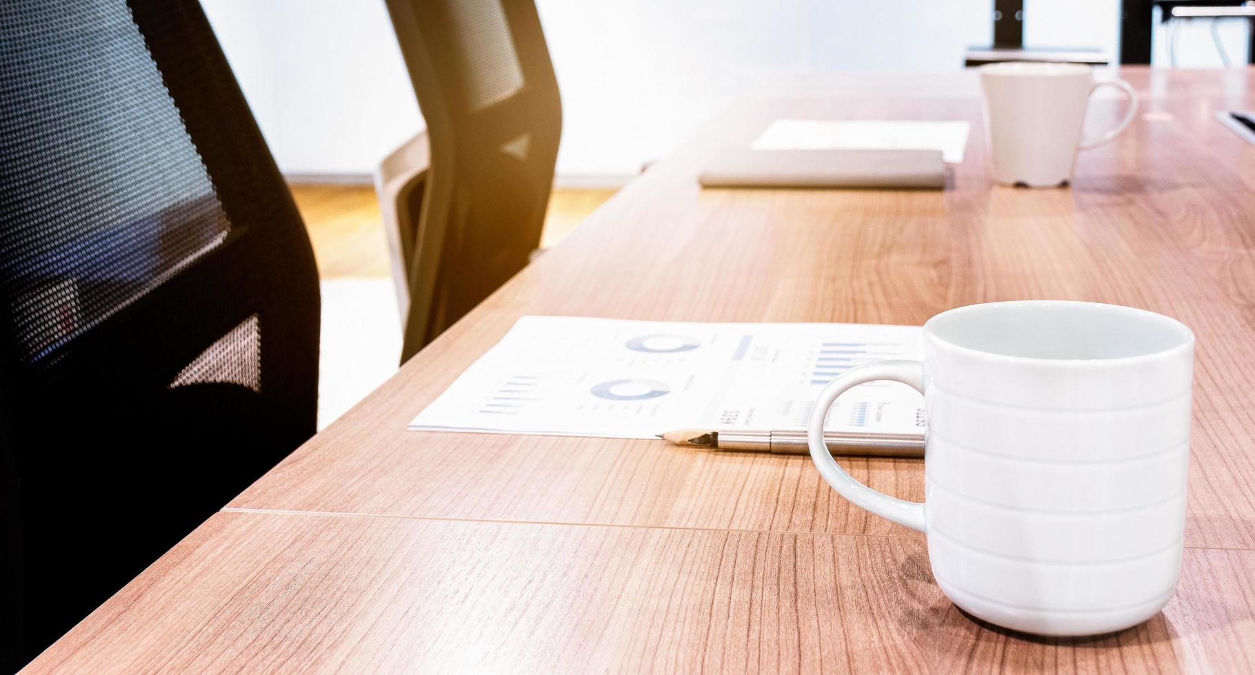 taza de café, papeleo y cuaderno en la mesa con dos sillones negros en la sala de reuniones foto