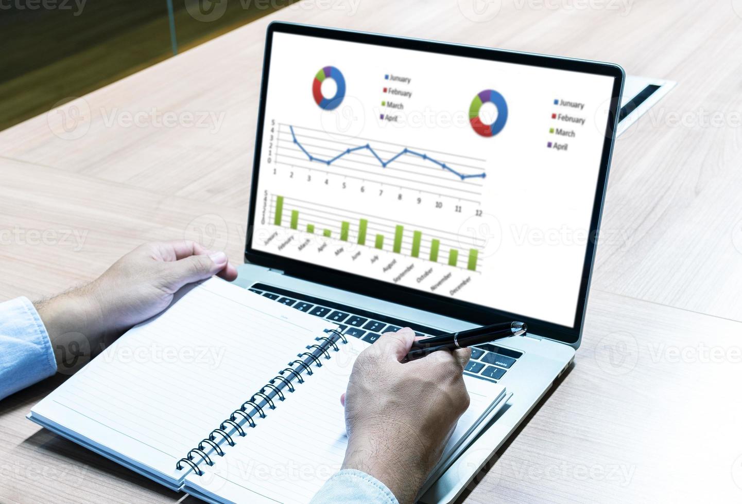 Businessman hand holding pen to take note on notebook with laptop display show slide presentation photo