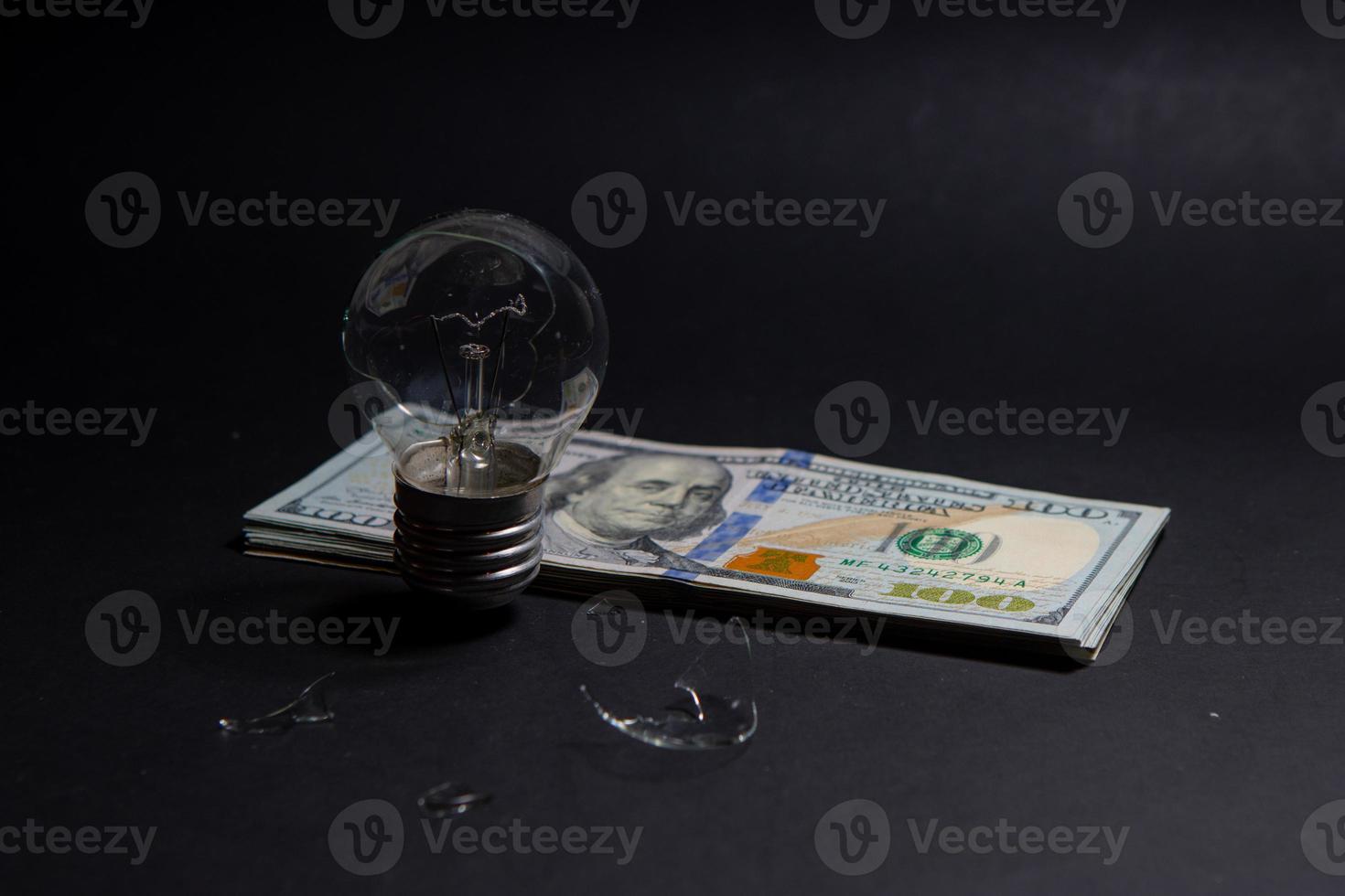bombilla rota con trozos de vidrio en billetes de 100 dólares. concepto de precios de la electricidad y la crisis de la electricidad en el mundo foto