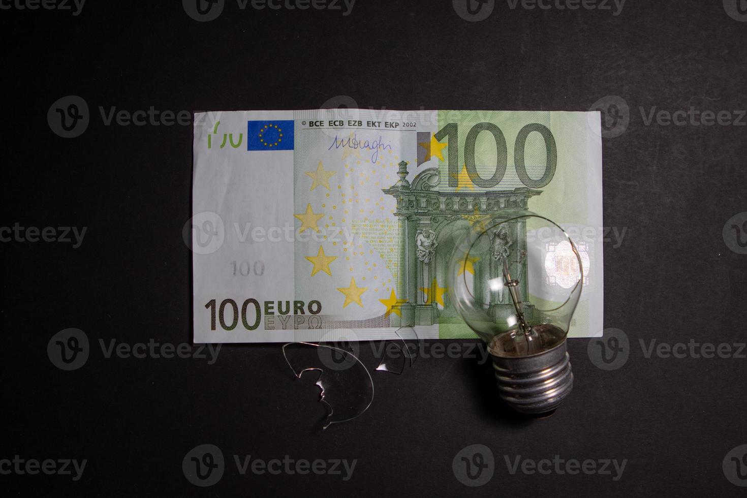 bombilla rota con trozos de vidrio en el billete de 100 euros. concepto de precios de la electricidad y la crisis de la electricidad en europa foto