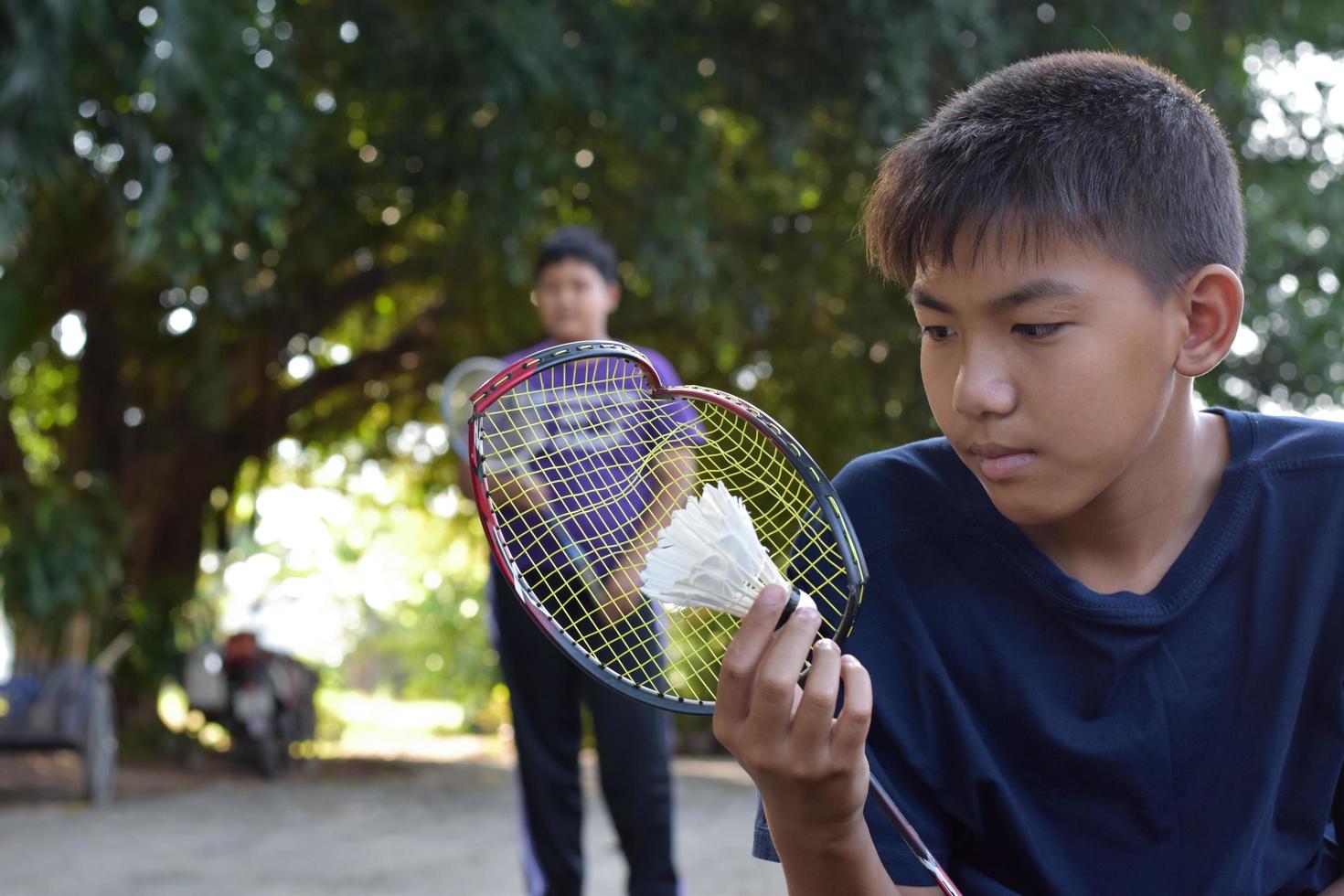 Young asian boy holds broken frame badminton racket in hand sadly while he is playing badminton with his friend outside the house, outdoor badminton concept, soft and selective focus. photo